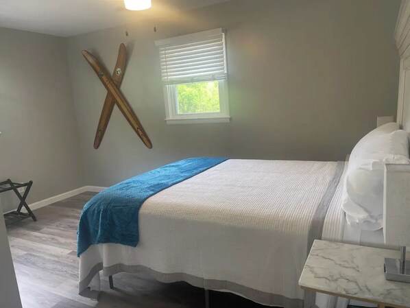 Un dormitorio con cama, ventana con persianas, un esquirol de madera y una mesita de noche con lámpara.