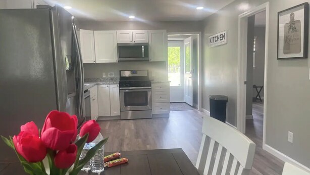 Une cuisine moderne avec des meubles blancs, des appareils en acier inoxydable et un coin repas comprenant une table en bois foncé et des chaises blanches.