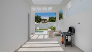 Un patio exterior moderno con piscina, una parrilla y sillas de descanso.