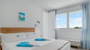 Un dormitorio con cama, una banca, una ventana con cortinas y un cuadro en la pared.