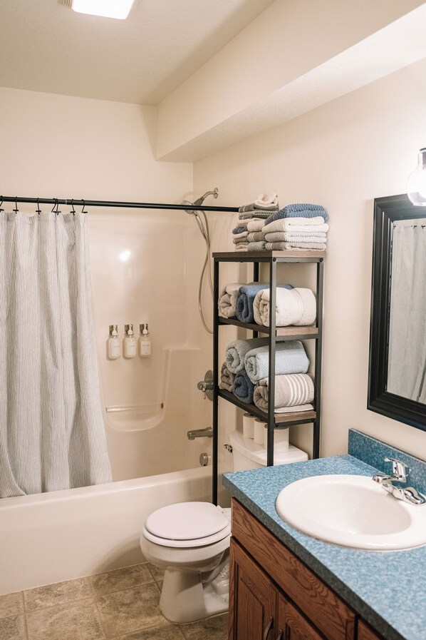 A bathroom with a bathtub, toilet, and a shelf with towels.