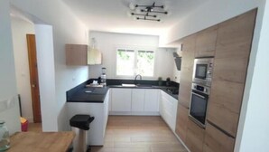 A compact kitchen with white cabinets, a black countertop, and a wooden floor. - Large villa with all comforts, secure swimming pool, garden and barbecue (Latour bas elne)