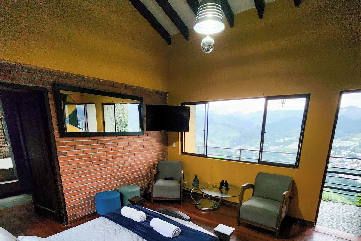 A room with a bed, a chair, a small table, and a TV mounted on the wall.