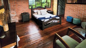 A bedroom with a brick wall, a large window, a bed, a nightstand, a dresser, and a chair. - CasaView (Manizales)