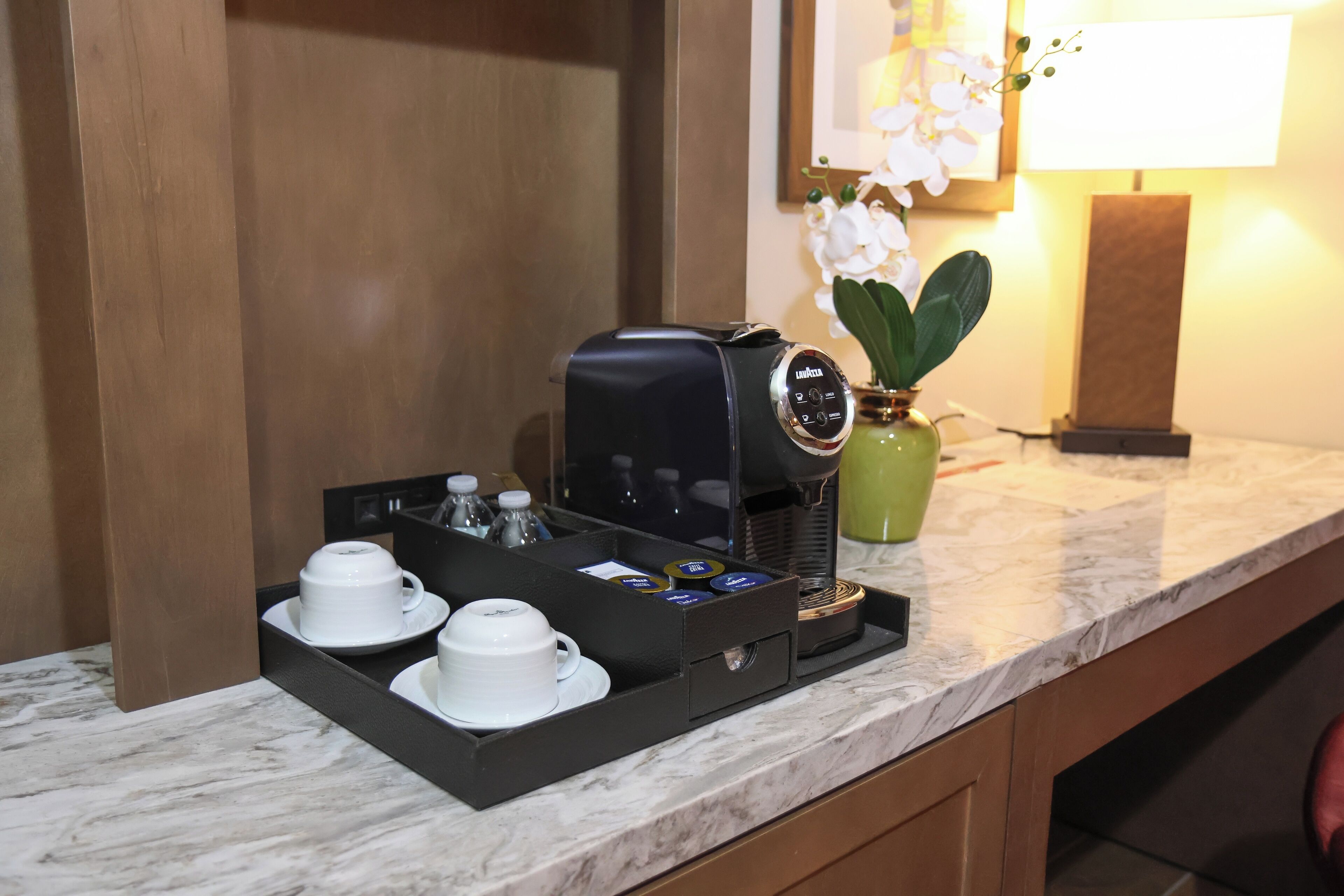 Una cafetera con una bandeja de tazas y condimentos sobre una encimera de mármol en una habitación de hotel.