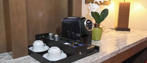 Una cafetera con una bandeja de tazas y condimentos sobre una encimera de mármol en una habitación de hotel.