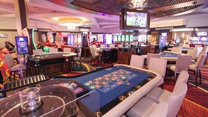A casino with slot machines, blackjack tables, and a large screen displaying a sports event. - Seminole Brighton Bay Hotel & Casino (Okeechobee)