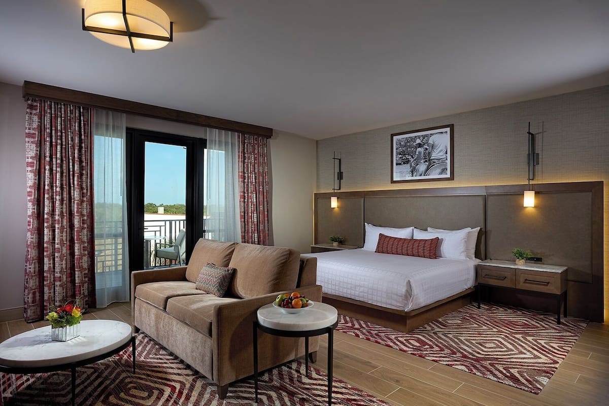 A hotel room with a bed, a sofa, a small table, and a view of the outdoors.