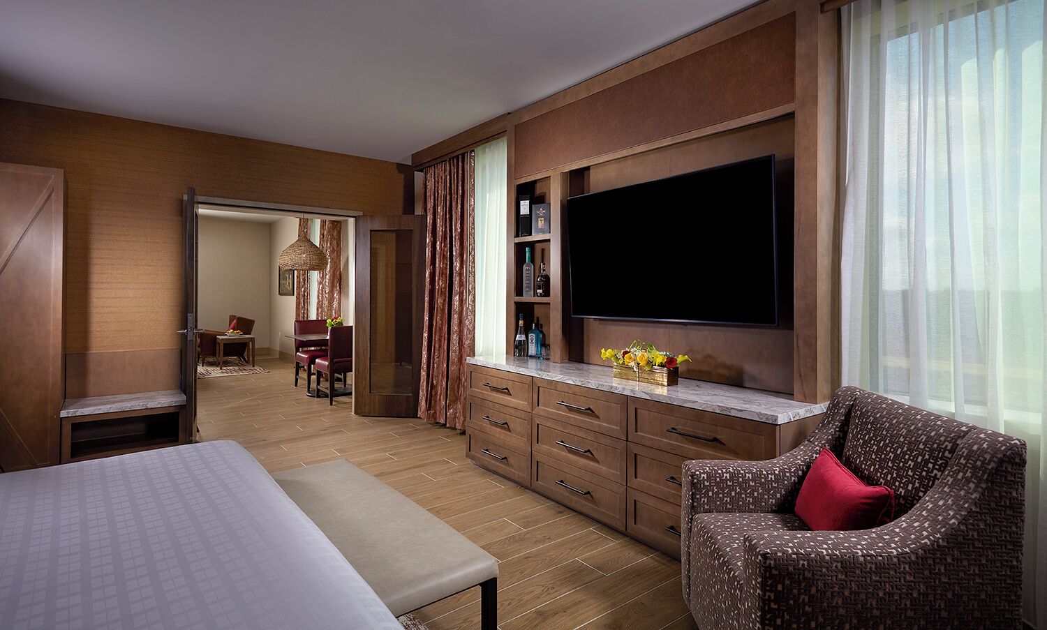 A hotel room with a large flat-screen TV, a dining area with a table and chairs, a sofa, and a minibar.
