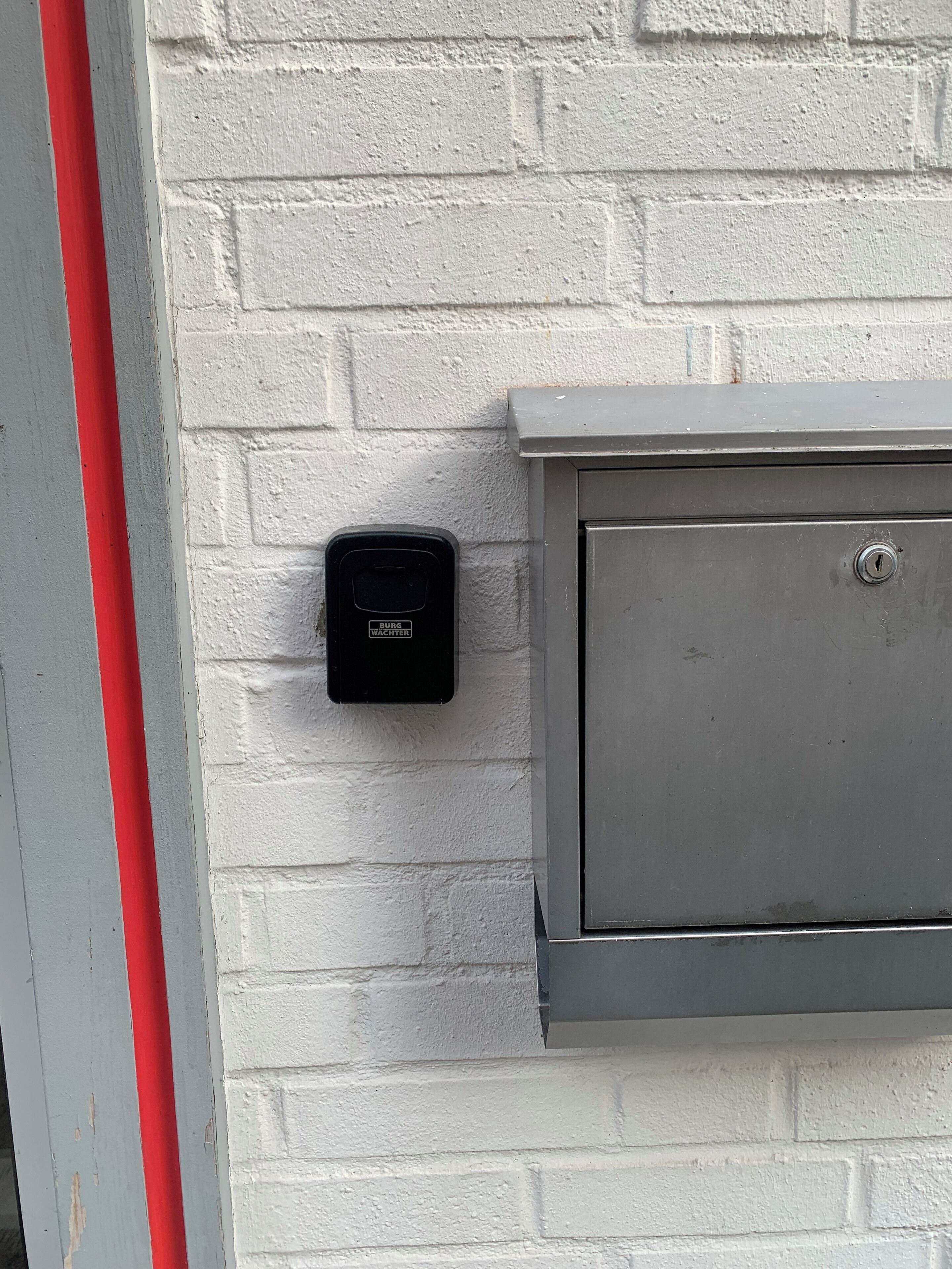 En elcentral monterad på en vit tegelvägg, med ett rött rör till vänster.
