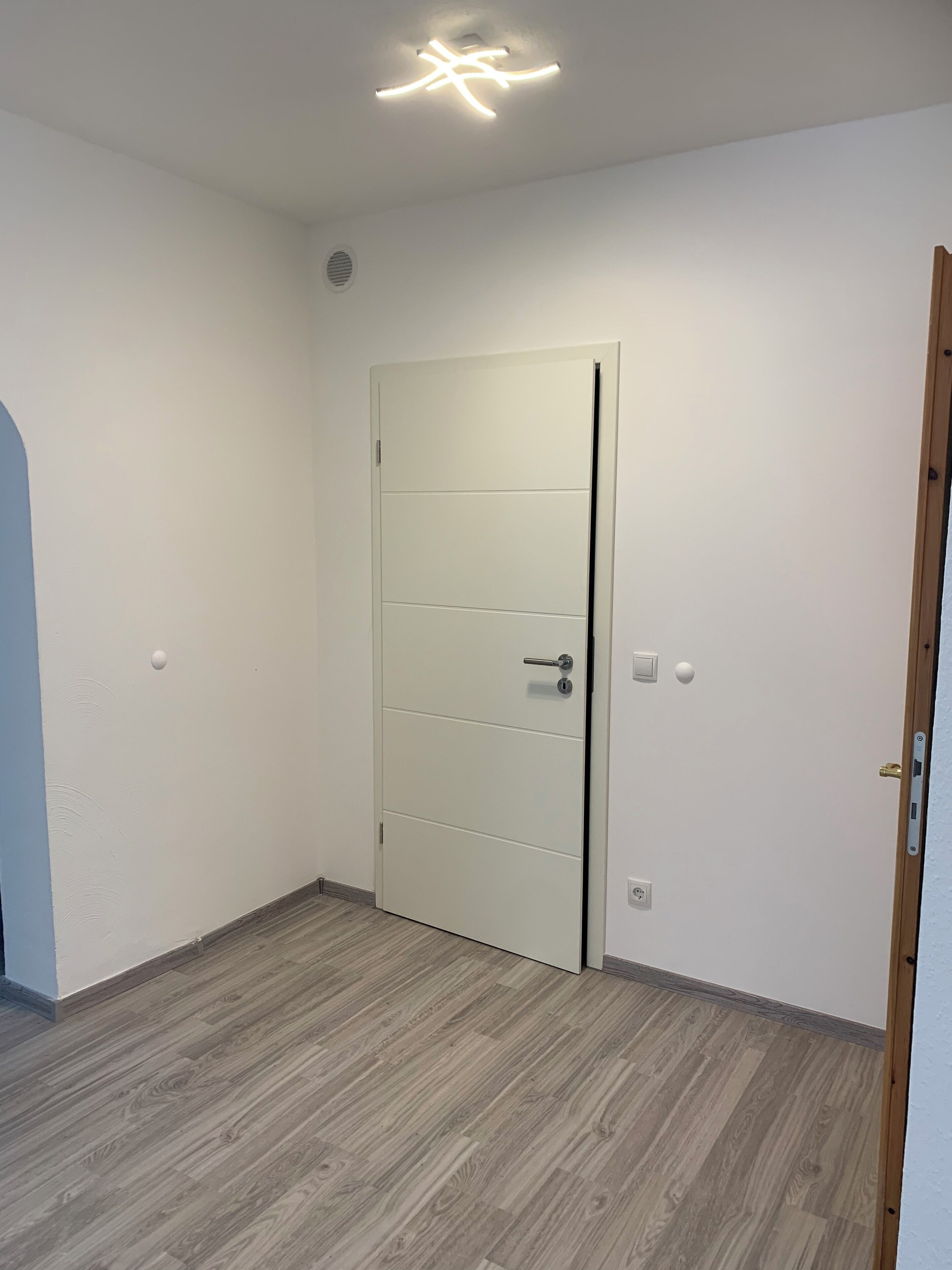 Une pièce avec une porte blanche, un interrupteur et un luminaire au plafond.