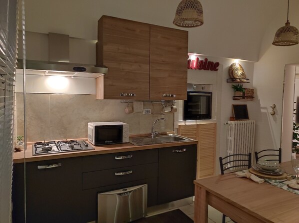 A compact kitchen with a built-in microwave, gas stove, and a small oven. There is a wooden cabinet above the sink and a small refrigerator below. - Li Brilli bed and breakfast (Alliste)