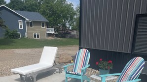 Un patio con dos sillas Adirondack, una silla de lounge y un brasero de metal.