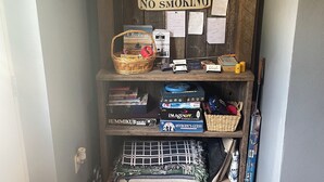Un rincón con un estante de madera que contiene varios objetos, incluyendo un cartel de 'No fumar', una cesta y juegos de mesa.