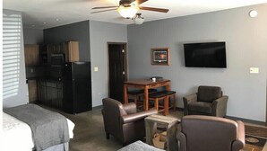 Habitación de hotel compacta con kitchenette, una cama, zona de estar con mesa y sillas, y televisor de pantalla plana montado en la pared.