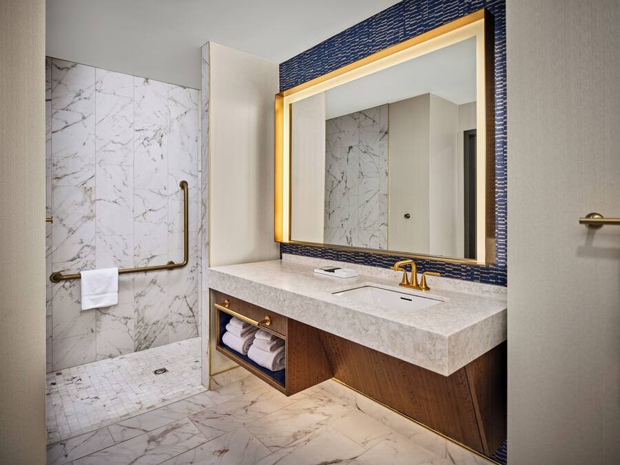 Un bagno moderno con pavimento in marmo, un grande specchio con cornice blu e un mobile lavabo con rubinetto dorato.
