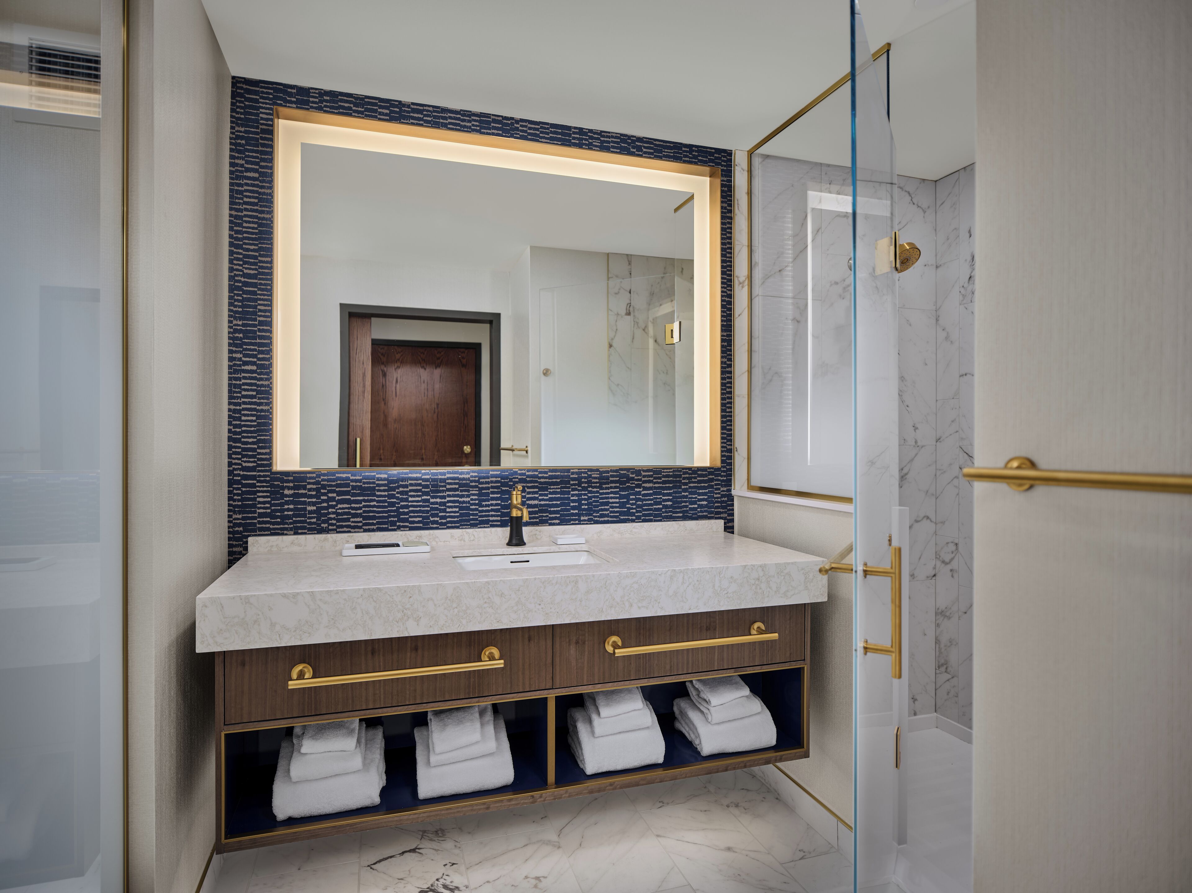 A modern bathroom with a marble sink, a large mirror, and a glass shower enclosure.