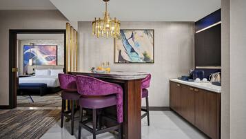 A modern hotel room with a dining area, a bed, and artwork on the walls.