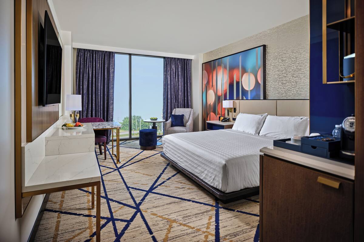 A hotel room with a large bed, a desk, a chair, a TV, and a view of the outdoors.