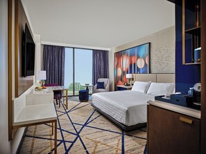 Habitación de hotel con una cama grande, un escritorio, una silla, un televisor y vistas al exterior.