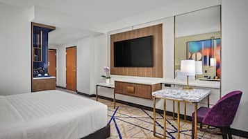 Habitación de hotel con cama, escritorio, televisor de pantalla plana, silla y un espejo grande.