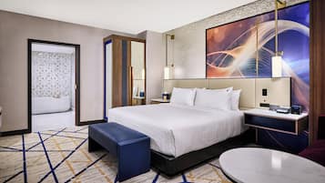 Een moderne hotelkamer met een groot bed, een nachtkastje met een lamp, een klein rond tafeltje en uitzicht op de stad door het raam.