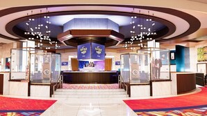 Un hall de hotel con una recepción central, vitrinas de cristal y un suelo cubierto de alfombra roja.