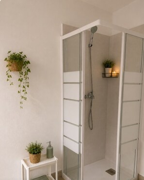 A glass-enclosed shower with a handheld showerhead, a small shelf with a plant, and a wall-mounted plant.