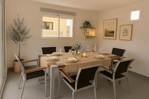 Un coin repas avec une table ronde dressée pour six personnes, entourée de chaises, d’une plante en pot et d’œuvres d’art encadrées accrochées au mur.