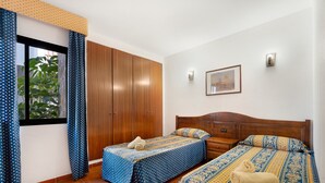 Un dormitorio con dos camas, un armario, una ventana con cortinas, un cuadro en la pared y suelo de baldosas.
