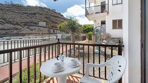 Un balcón con mesa y sillas, con vista a una carretera y una ladera.