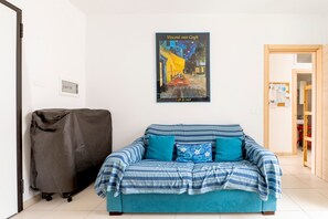 A room with a blue sofa, a covered chair, and a wall-mounted poster of Vincent van Gogh's 'Café de Nuit'.