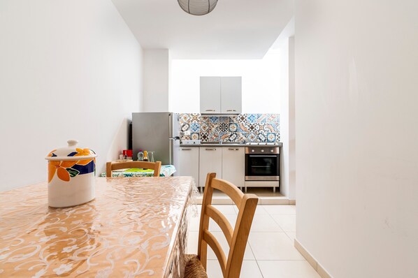 A compact kitchen with white cabinets, a tiled backsplash, and a dining area with a table and chairs.