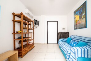 A room with a wooden bookshelf, a television, a striped sofa, and a painting on the wall.