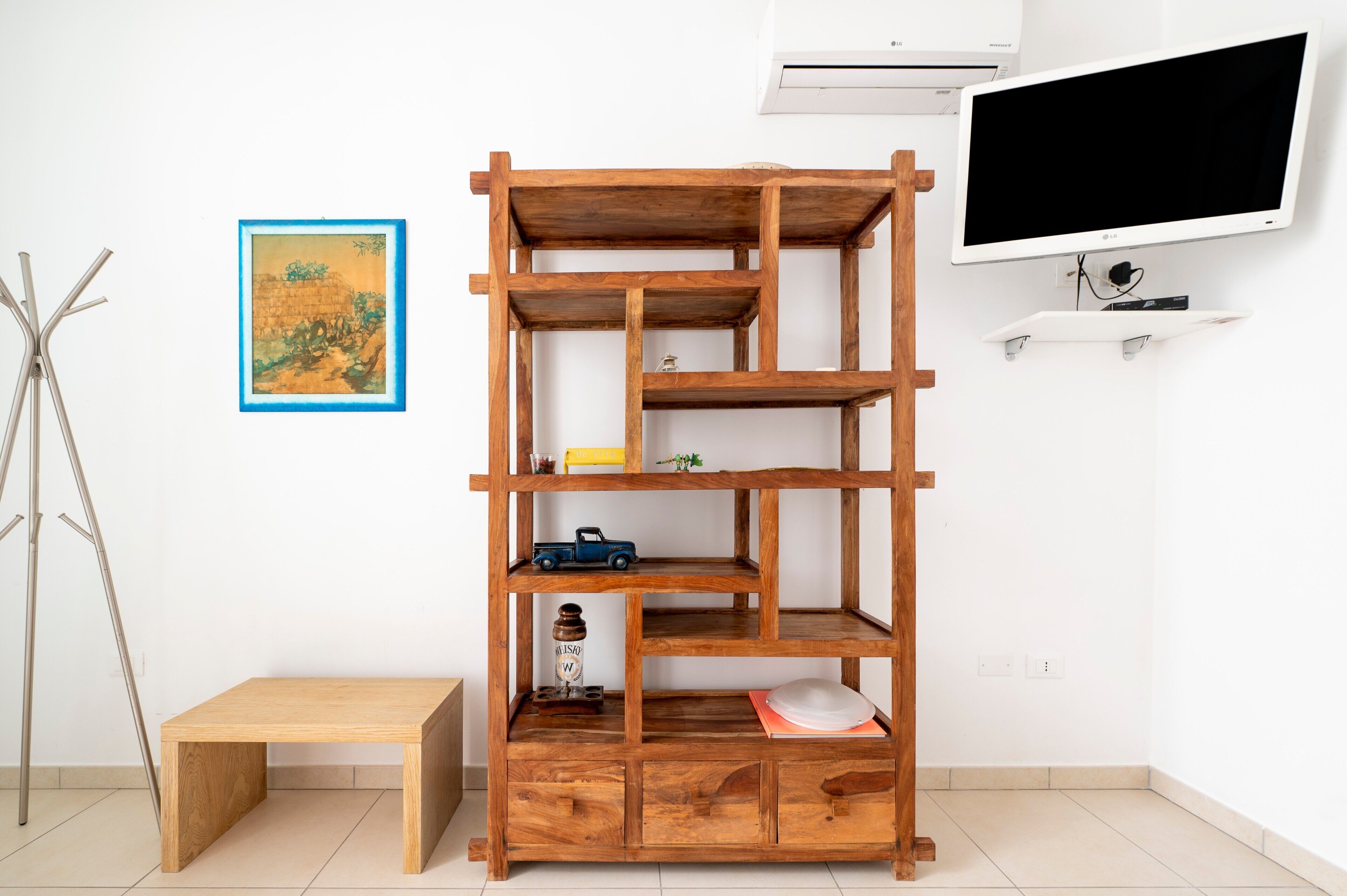 A wooden shelf unit with multiple shelves, a small bench, and a framed picture on the wall.