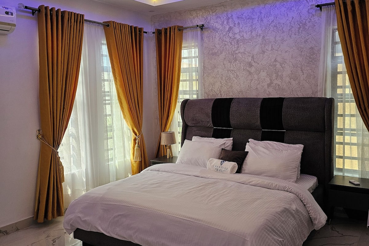 Ein modernes Schlafzimmer mit einem großen Bett, einer Deckenleuchte und einem Fenster mit Vorhängen.