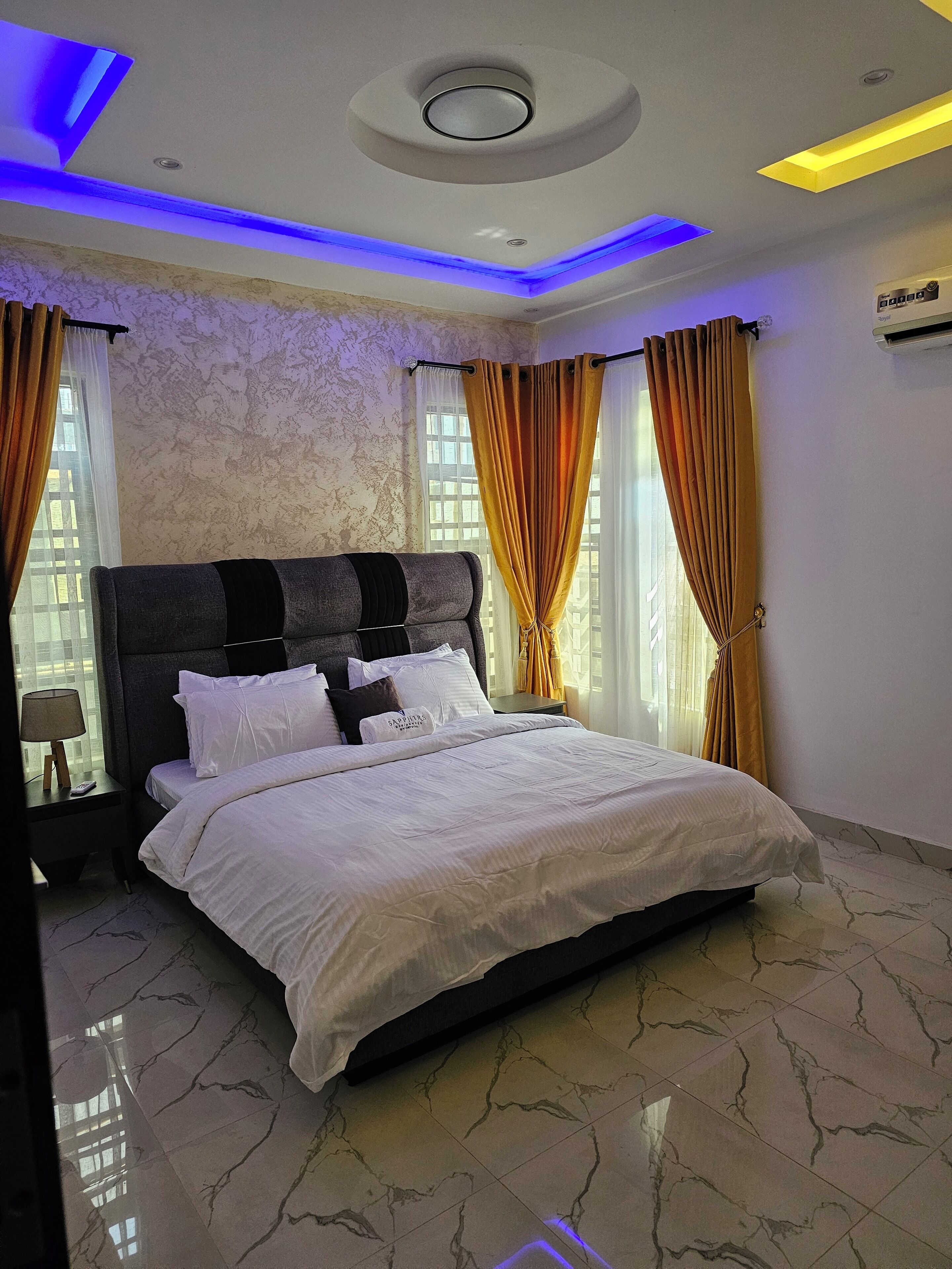 A modern bedroom with a large bed, marble flooring, and a ceiling with integrated lighting.