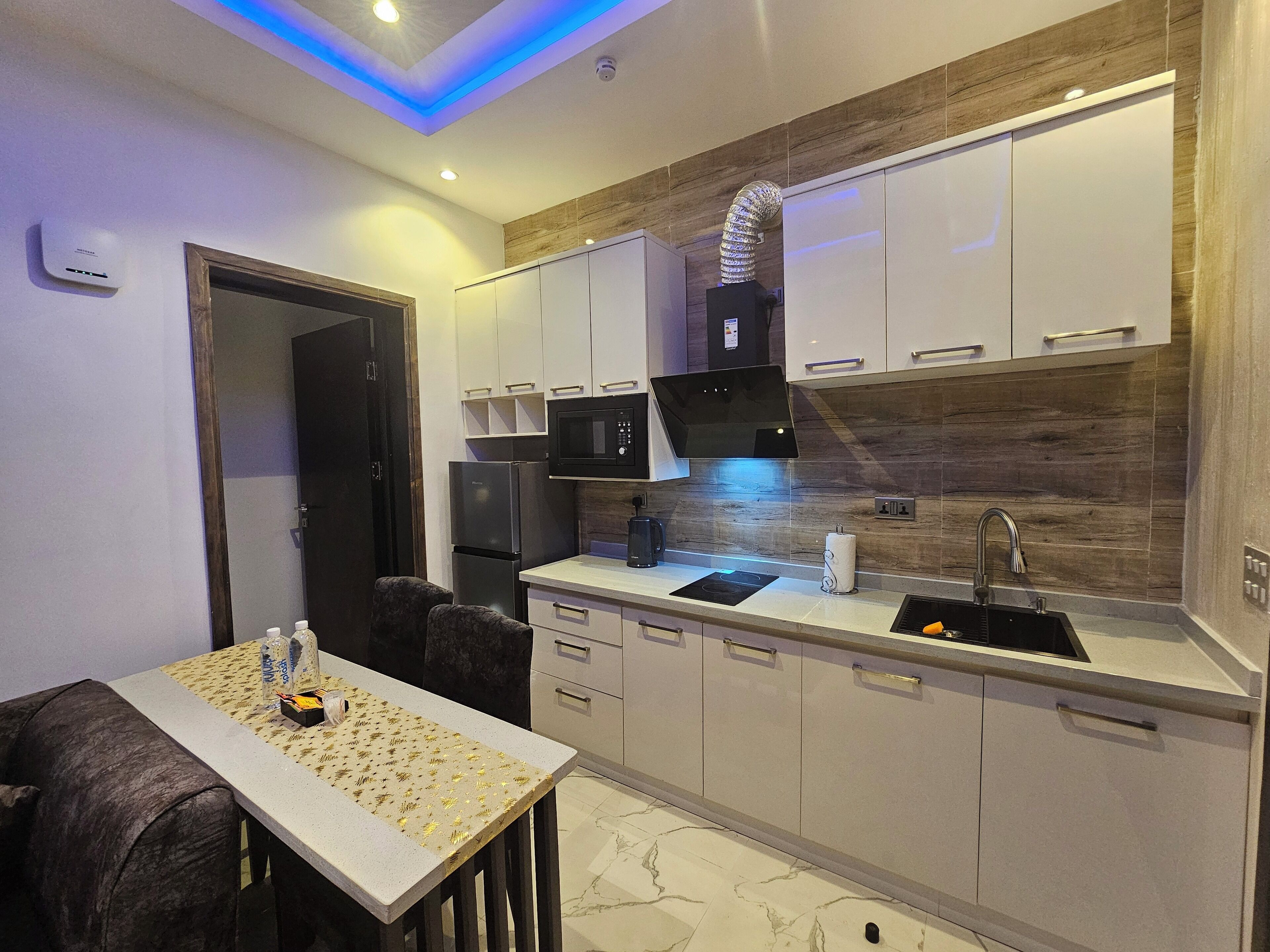 A modern kitchen with white cabinets, a black microwave, and a built-in oven. There is a dining table with chairs and a small island with a sink.