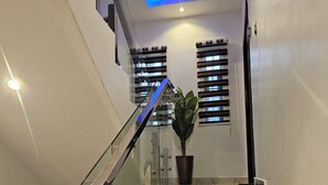 A modern staircase with glass railings, a potted plant, and a blue-lit ceiling.