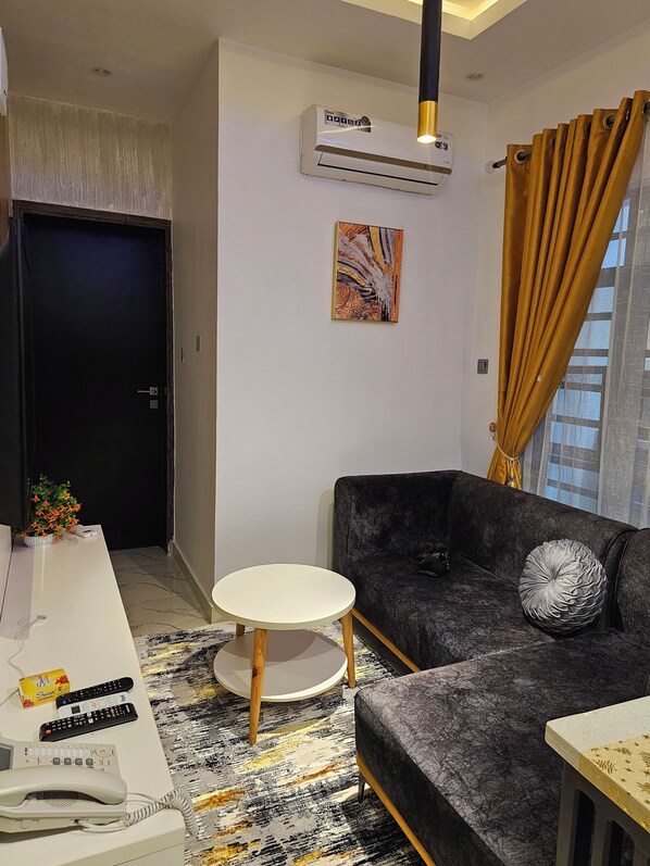 A modern living room with a dark grey sofa, a small white table, a decorative rug, and a painting on the wall.