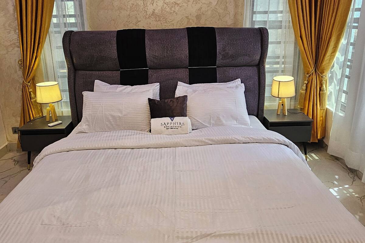 Ein großes Bett mit Kopfteil, zwei Nachttische mit Lampen und ein Schild am Kopfteil.