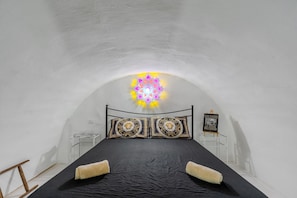 Una habitación estrecha y con arco, con una cama, almohadas y una lámpara decorativa.