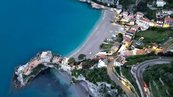 An aerial view of a coastal town with a winding road, buildings, and a beach.