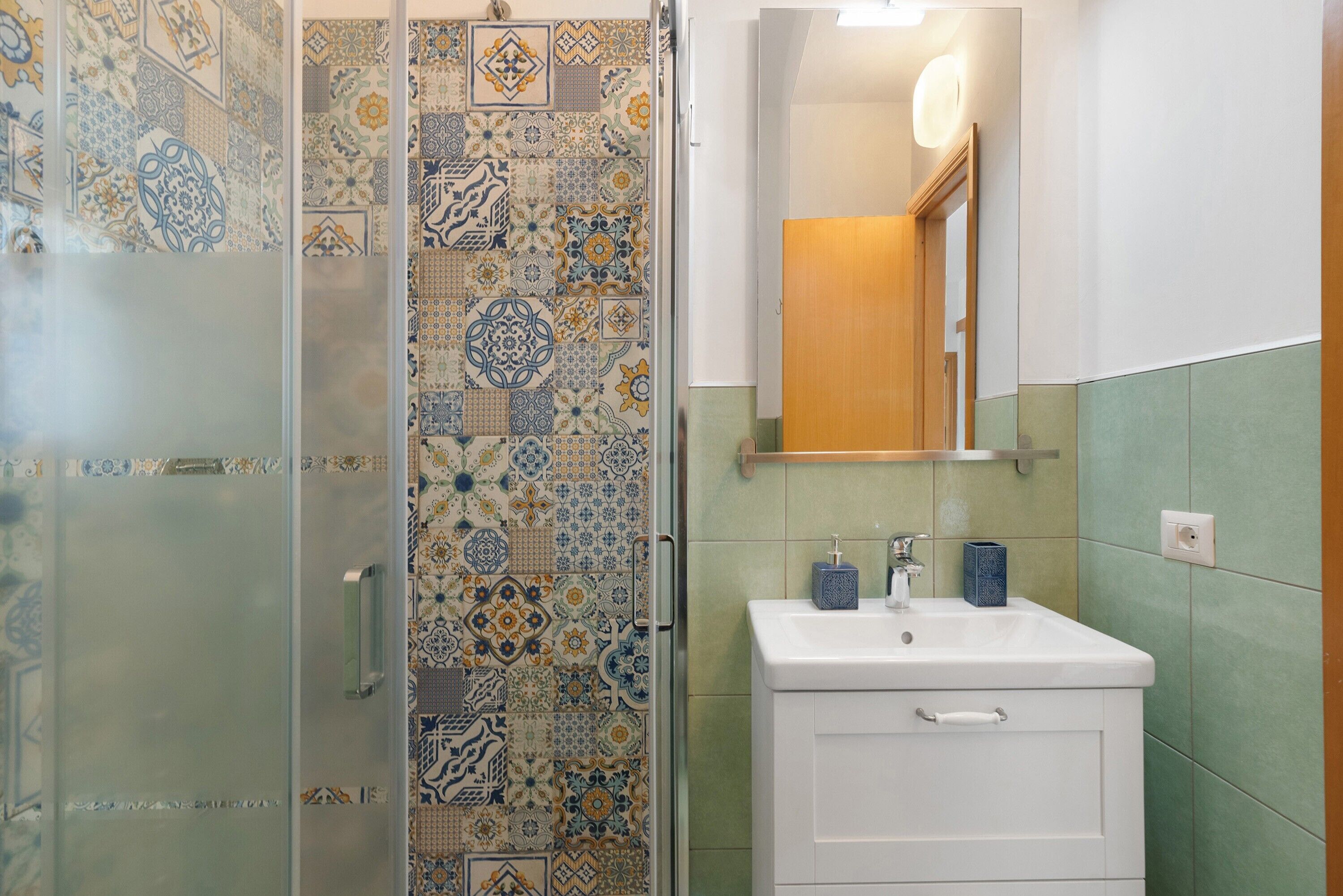 A bathroom with patterned tiles, a glass shower enclosure, a white sink, and a mirror.