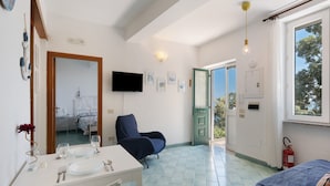 Une pièce comprenant une table à manger dressée pour deux personnes, une chaise, un lit, un téléviseur et une porte donnant sur l’extérieur.