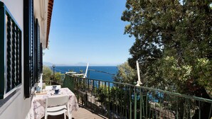 Un balcon avec une table et des chaises, offrant une vue sur la côte, avec des arbres et une balustrade.