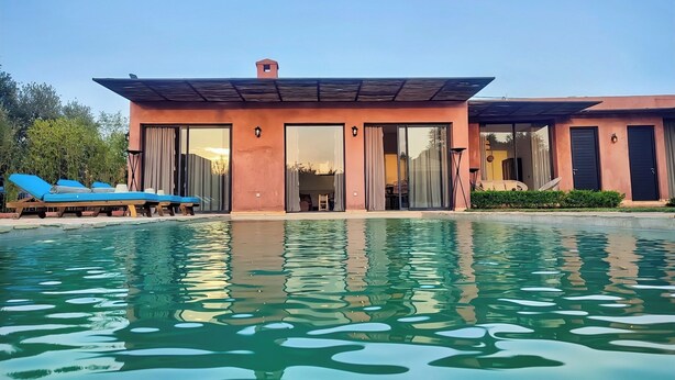 A modern house with a swimming pool, large sliding glass doors, and blue lounge chairs. - Domaine Homa in Marrakech: A Haven of Peace and Relaxation (Marrakech)