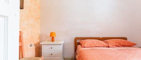 A bedroom with a bed, a nightstand, a lamp, a chair, and patterned floor tiles.
