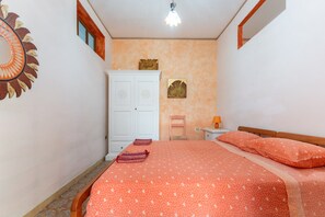A bedroom with a bed, a wardrobe, a nightstand, a lamp, and a wall decoration.