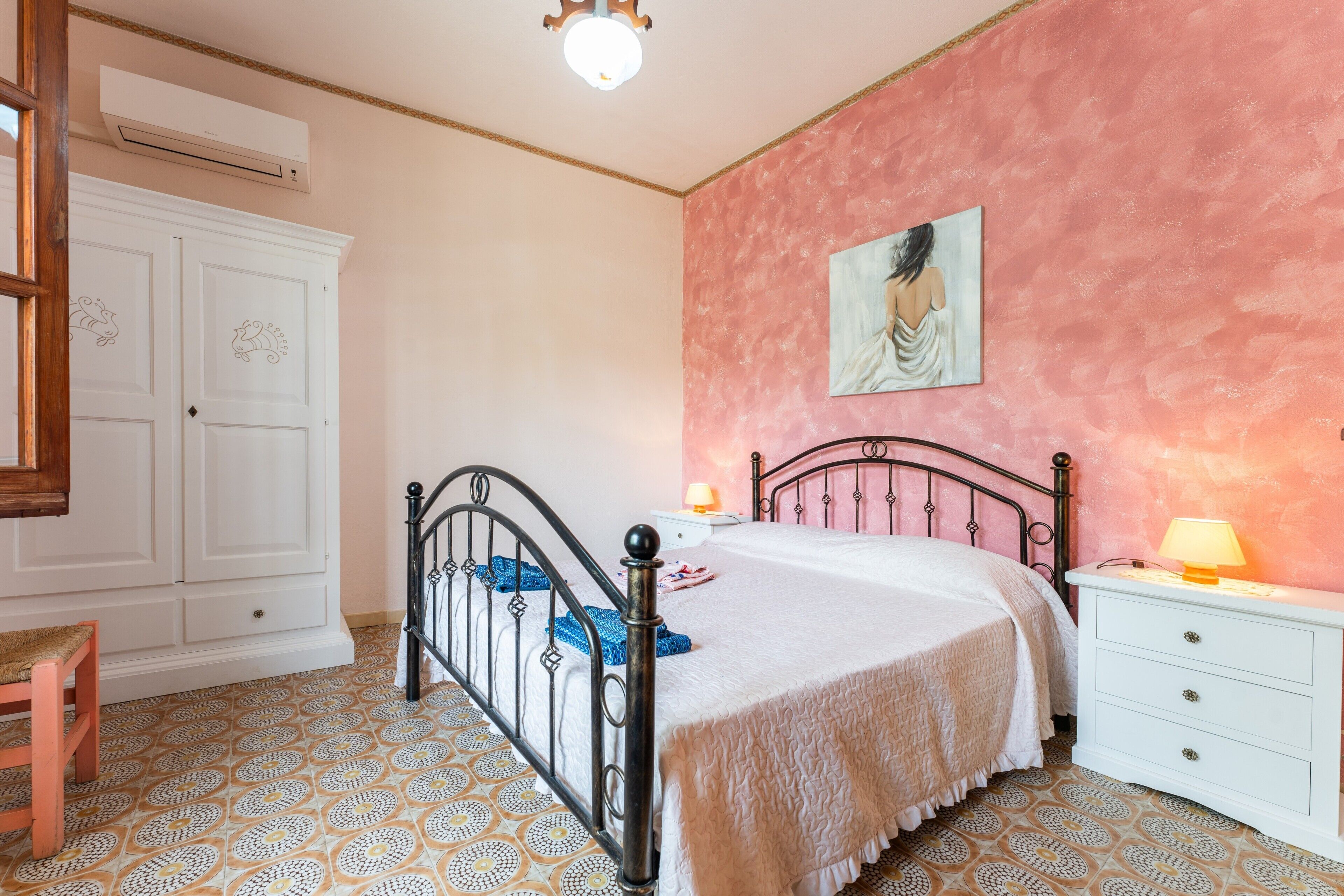 A bedroom with a bed, a nightstand, a dresser, a wardrobe, and a painting on the wall.